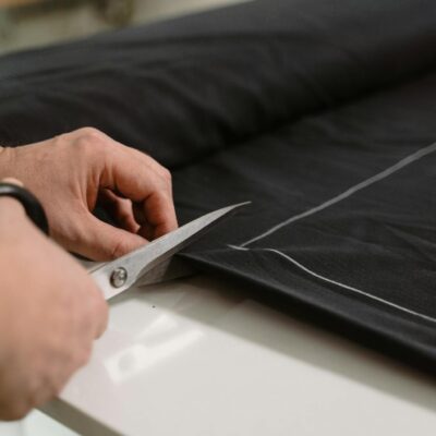 Close-up of a tailor's hand cutting black fabric with scissors, highlighting craftsmanship.